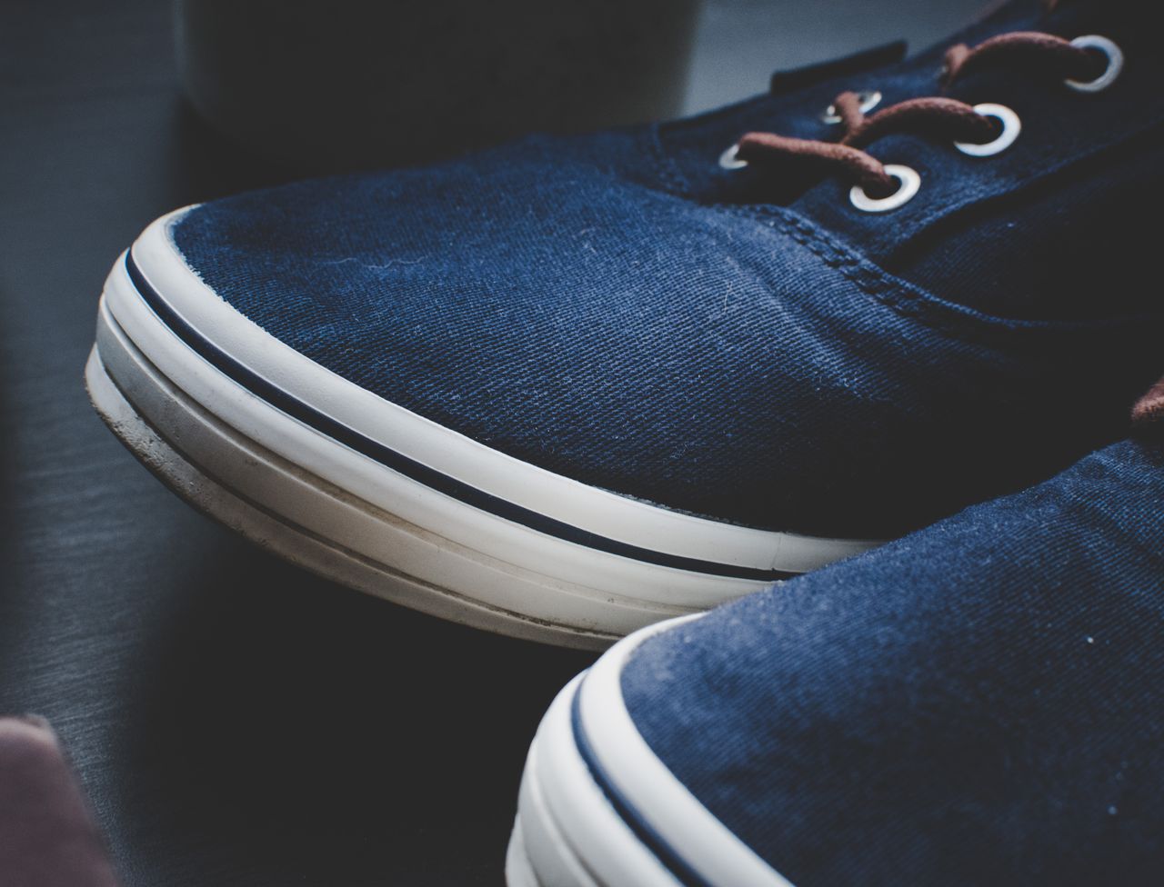 Detailed close-up of navy blue canvas sneakers with white soles on a black background.