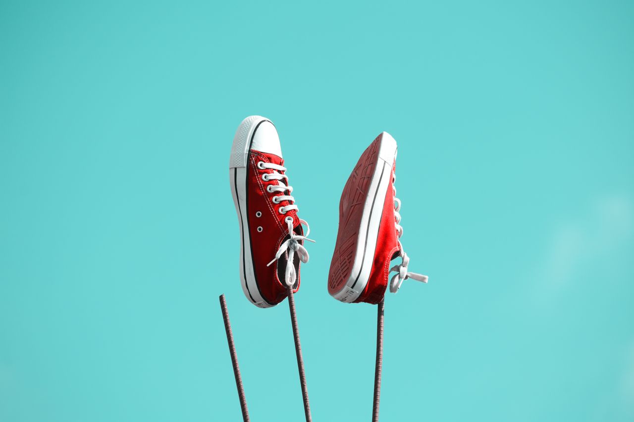 Services Red sneakers suspended against a vibrant blue sky, showcasing a playful and artistic vibe.