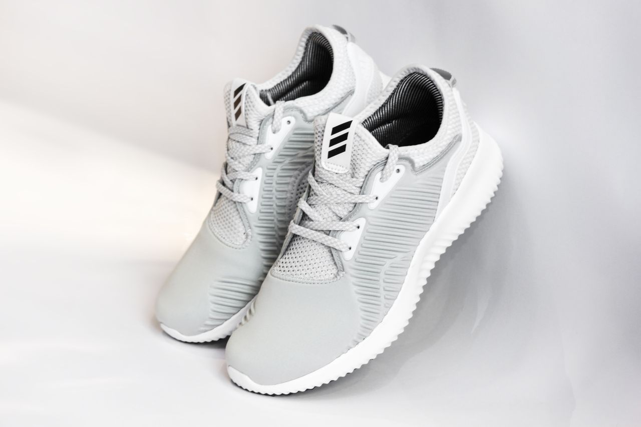 Services Pair of sports shoes with gray dense texture of surface and rubber inserts from sided and laces and white soles placed with heels up leaning on glance gray background