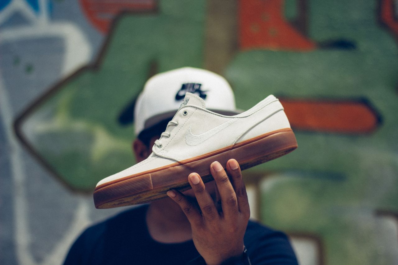Services Unrecognizable man in cap holding stylish white sneakers with rubber outsole in hand while standing against wall with graffiti