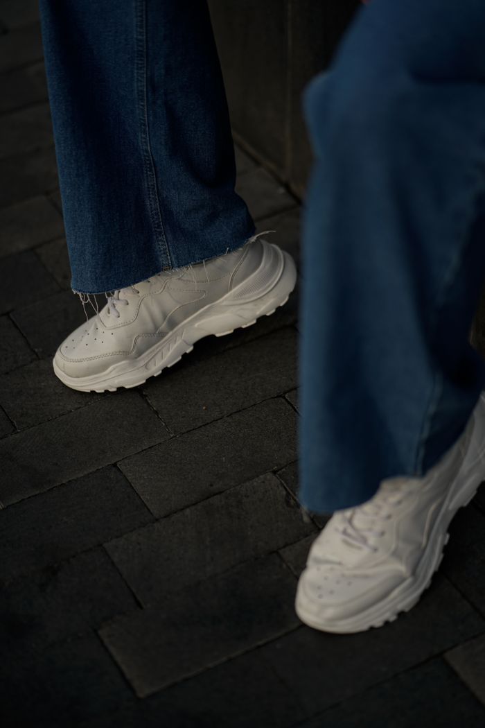 Services Close-up of stylish white sneakers paired with denim jeans on an urban street.