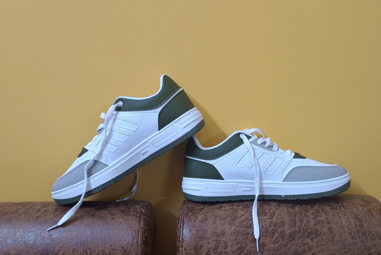 Services White and green casual shoes elegantly displayed against a yellow backdrop, perfect for fashion concepts.