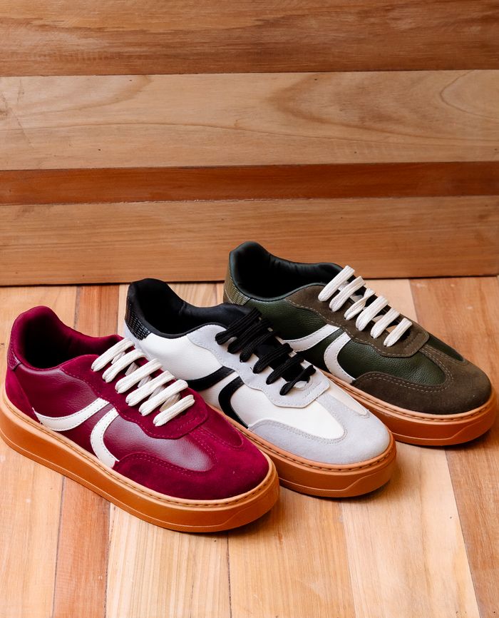 About Three pairs of trendy sneakers on a wooden floor offer a stylish footwear display.