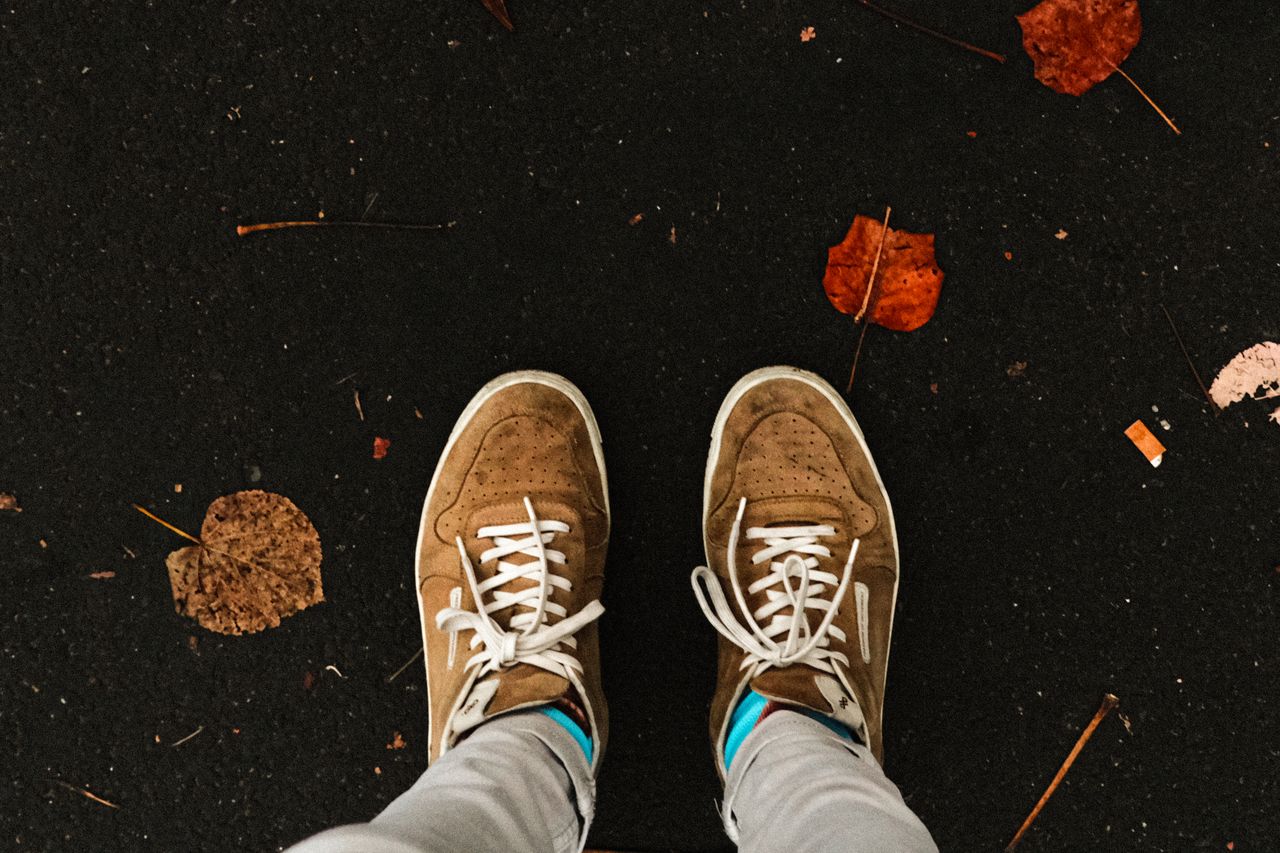 Services Brown sneakers on a dark pavement with scattered autumn leaves, embodying a fall vibe.
