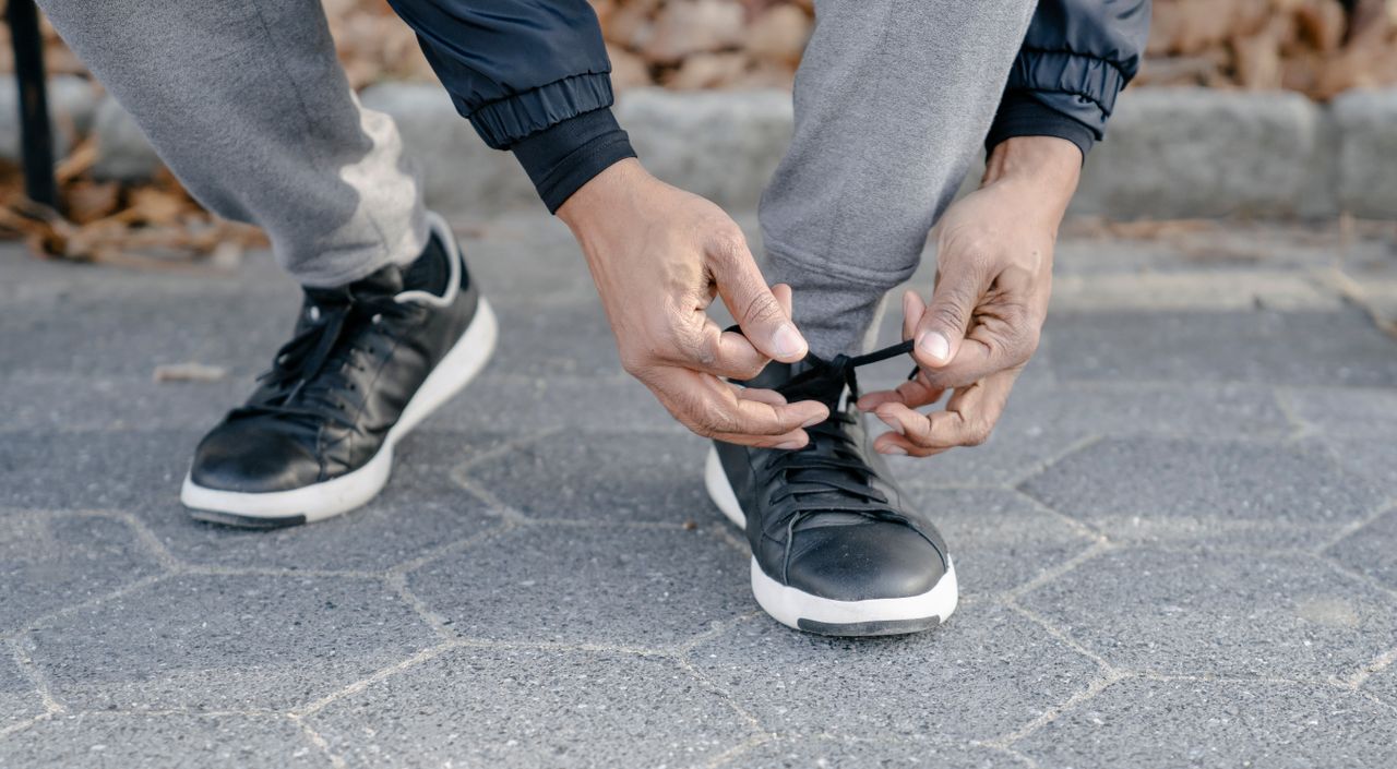 Services Crop unrecognizable African American person tying shoelace on sneakers while standing on cobblestone pavement